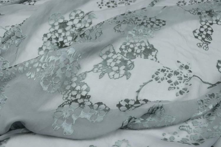a close-up view of a fabric with a floral pattern, featuring a mix of white and gray colors.