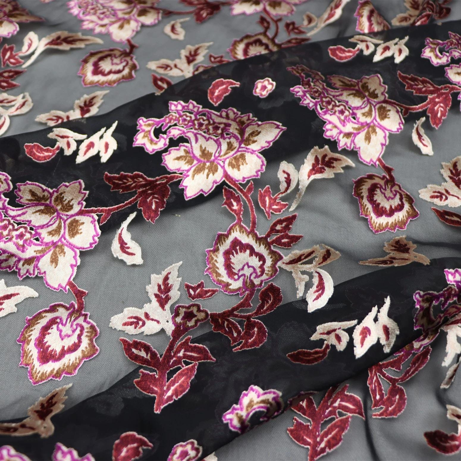 a close-up view of a fabric with a floral pattern in shades of red, pink, and white. The fabric appears to be a sheer material, with the pattern of flowers and leaves visible on the surface.