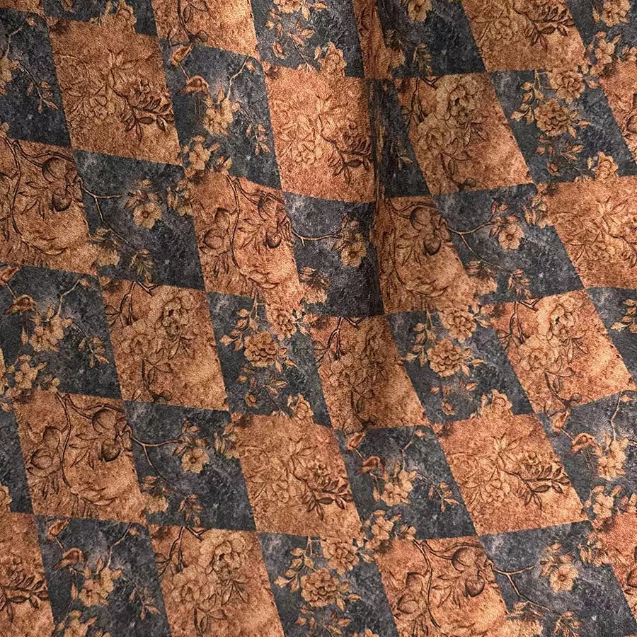 a close-up view of a fabric with a repeating pattern of floral designs in shades of brown and black. The pattern consists of diamond-shaped motifs with floral elements, creating a visually striking and intricate design.