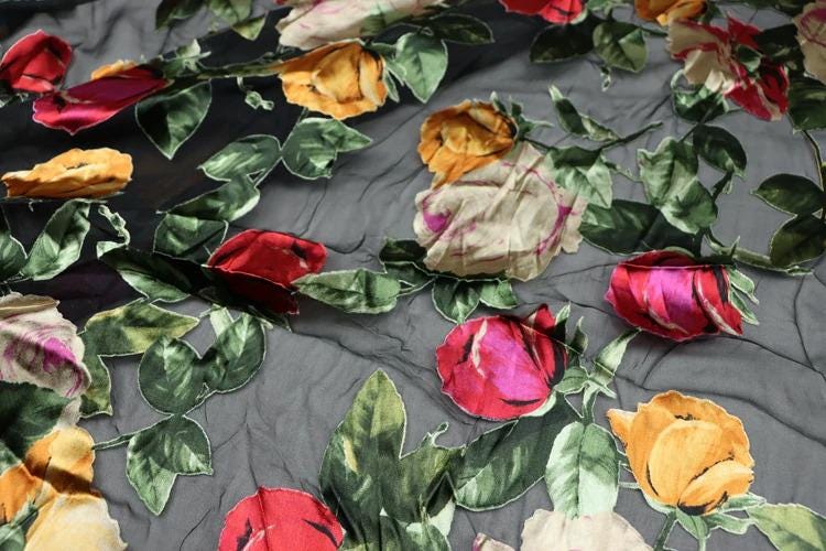 a close-up view of a fabric with a floral pattern, including red, yellow, and pink flowers. The fabric appears to be made of silk or a similar material, and the flowers are intricately embroidered or printed onto the fabric.