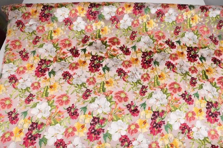 a fabric with a vibrant floral pattern, featuring a variety of colorful flowers in shades of red, white, yellow, and green. The pattern is spread across the fabric, creating a visually appealing and lively design.