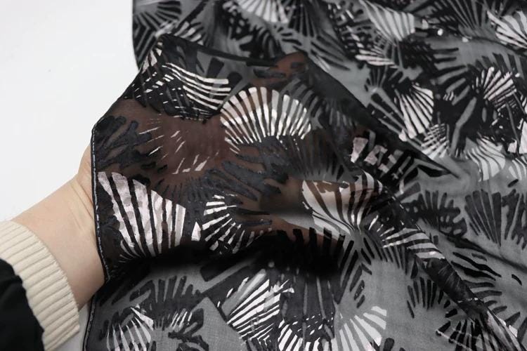 A hand is holding a black and white patterned fabric with a repeating fan-like design.