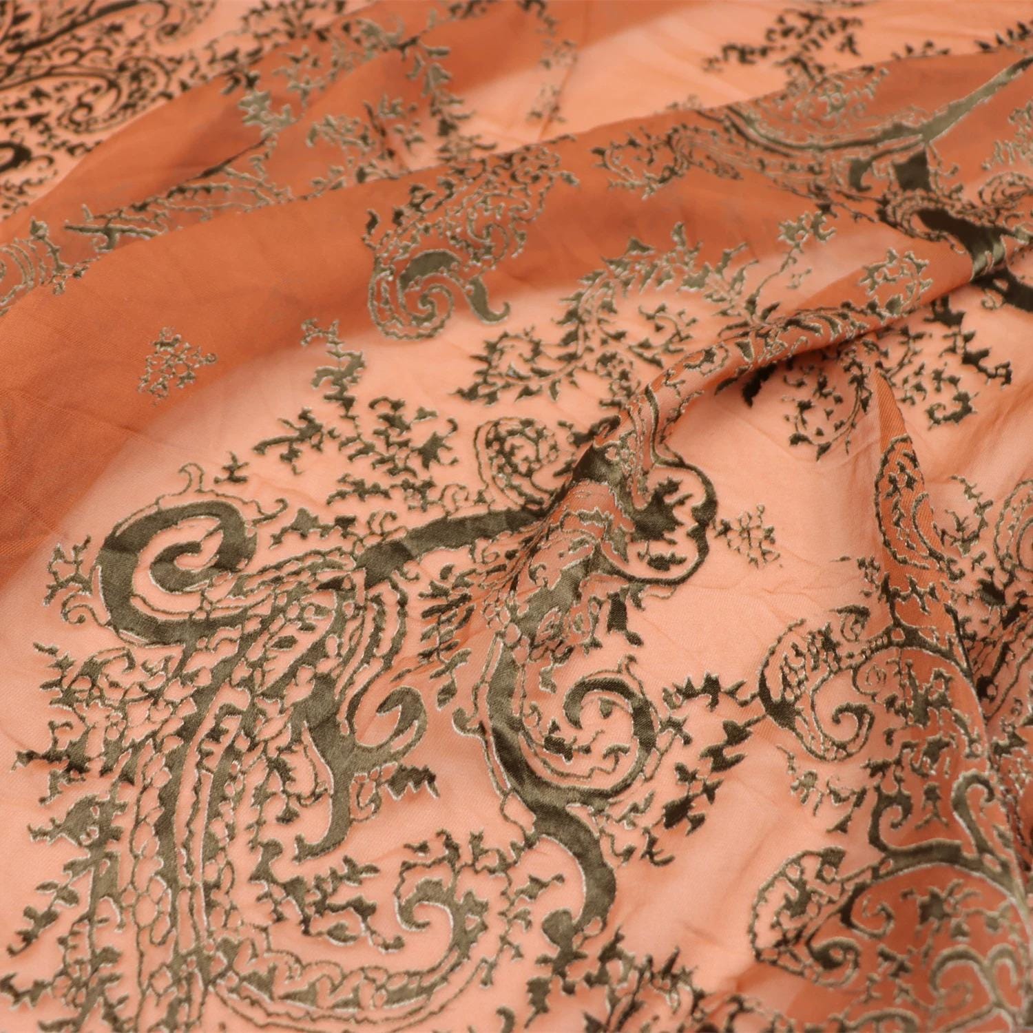 a close-up view of a fabric with a detailed, intricate paisley pattern in shades of orange and black.