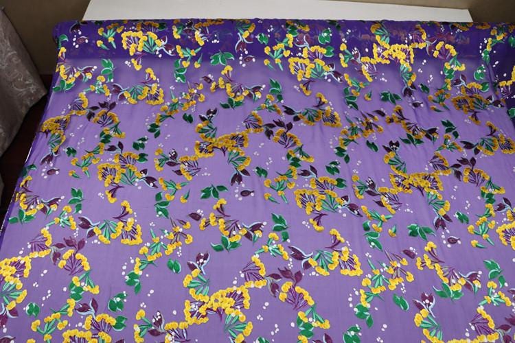 a vibrant purple fabric with a repeating pattern of yellow and green flowers and leaves. The fabric appears to be a large piece, covering a significant portion of the frame.