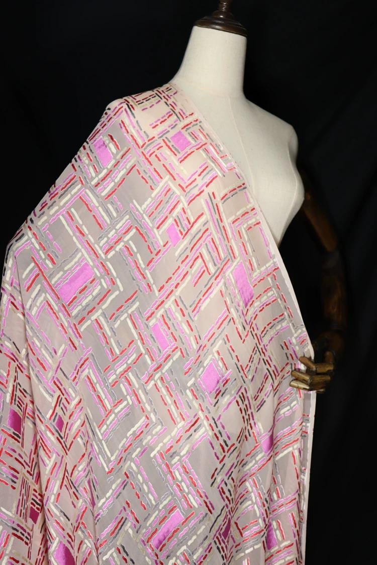 A mannequin wearing a white dress with a pink and white geometric patterned fabric draped over it.