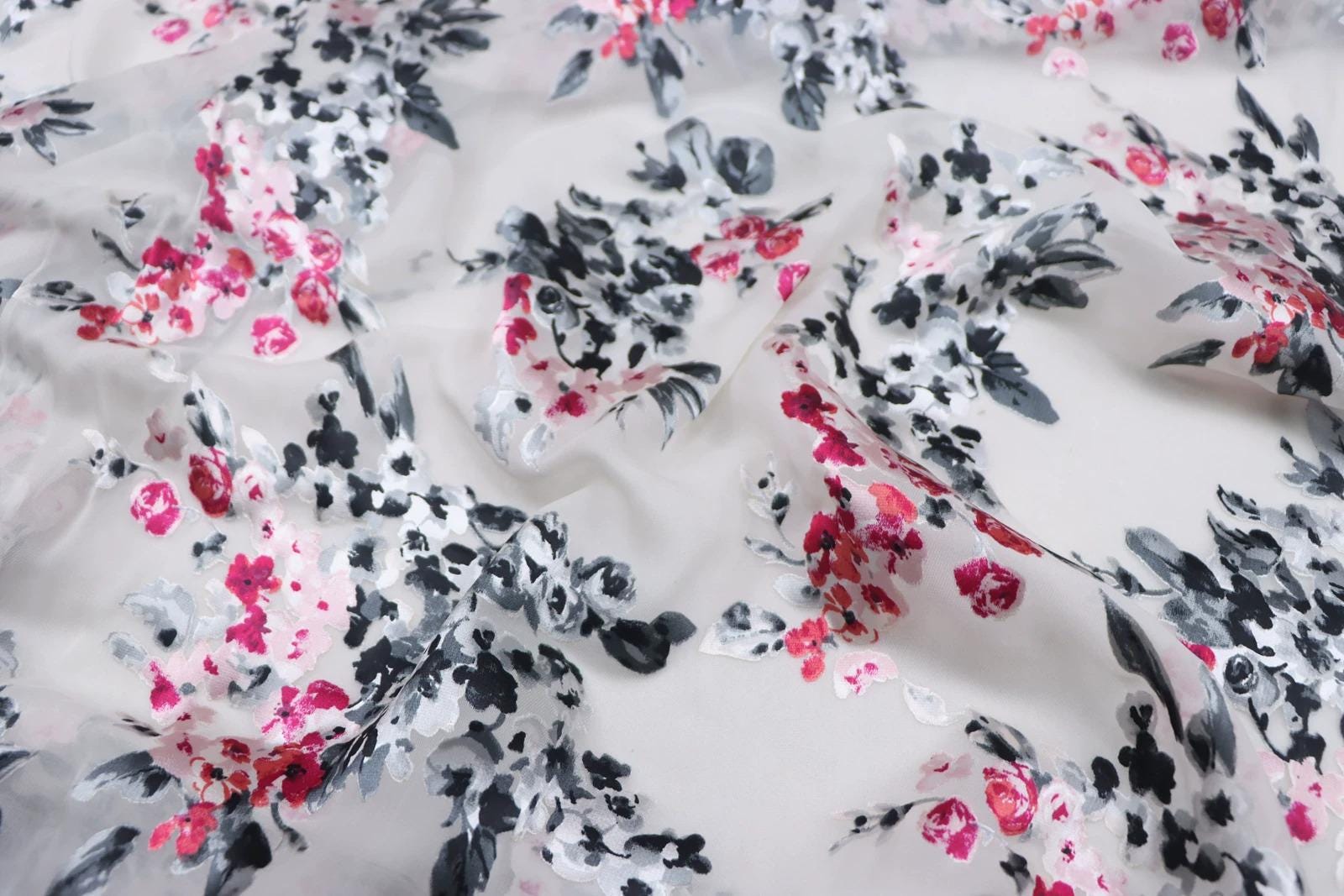 a close-up view of a fabric with a floral pattern in shades of pink, black, and white. The pattern appears to be a mix of different flowers and leaves, creating a visually appealing and intricate design.