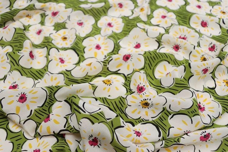 a close-up view of a fabric with a repeating pattern of white flowers with yellow centers against a green background.