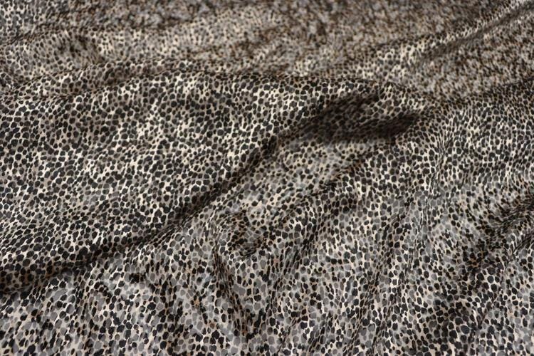 a close-up view of a fabric with a distinctive leopard print pattern. The fabric appears to be made of a material with a textured, spotted appearance, resembling the fur of a leopard.