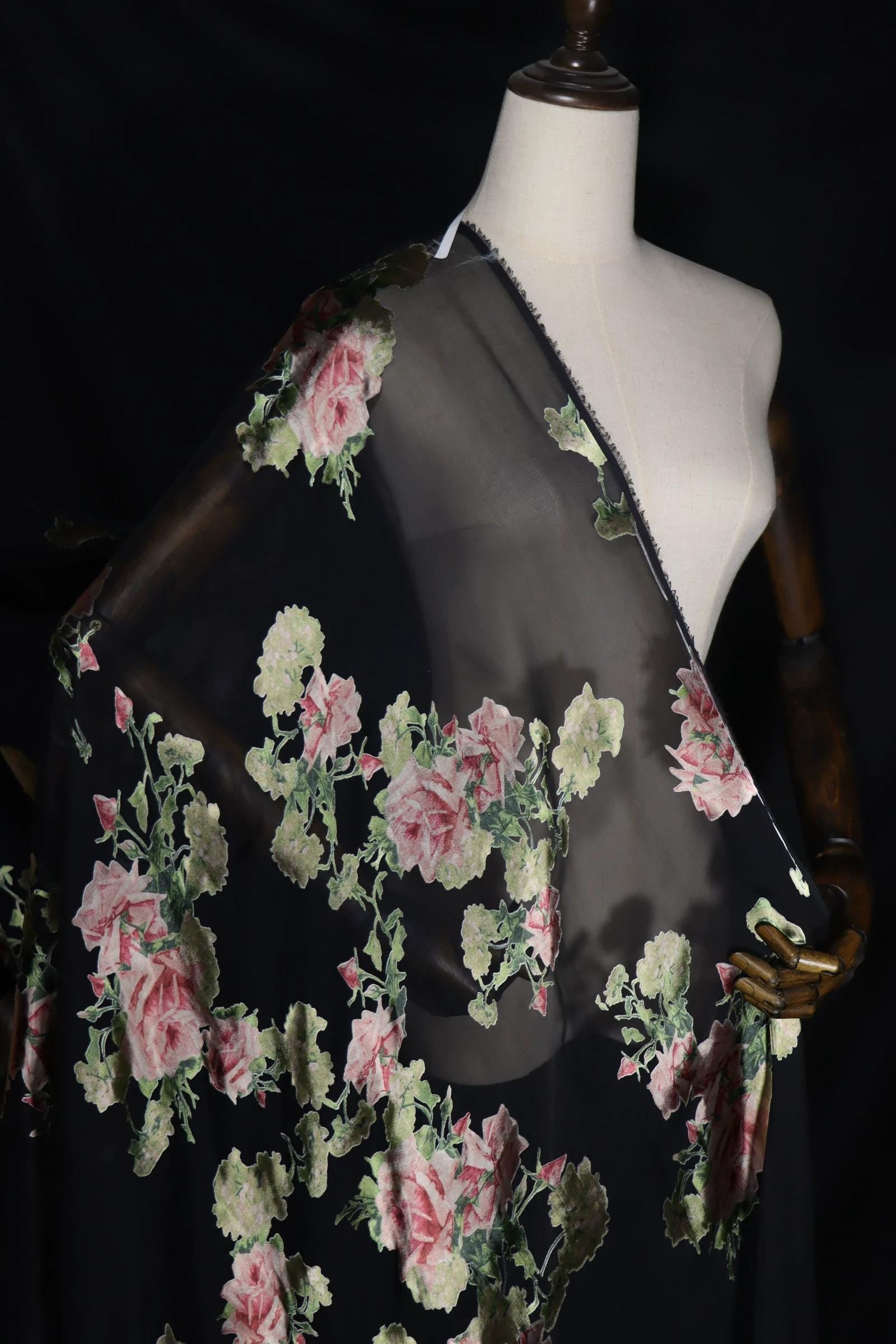 A mannequin wearing a black dress with a floral print, featuring pink and green flowers.
