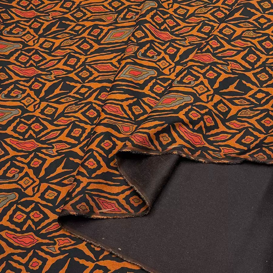 a close-up view of a fabric with a vibrant, geometric pattern in shades of orange and black. The pattern consists of various shapes and designs, creating a visually striking and intricate design.