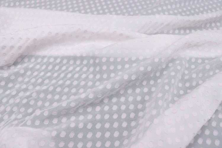 a close-up view of a fabric with a white polka dot pattern. The fabric appears to be a sheer material, with a crumpled texture that gives it a soft and delicate appearance.