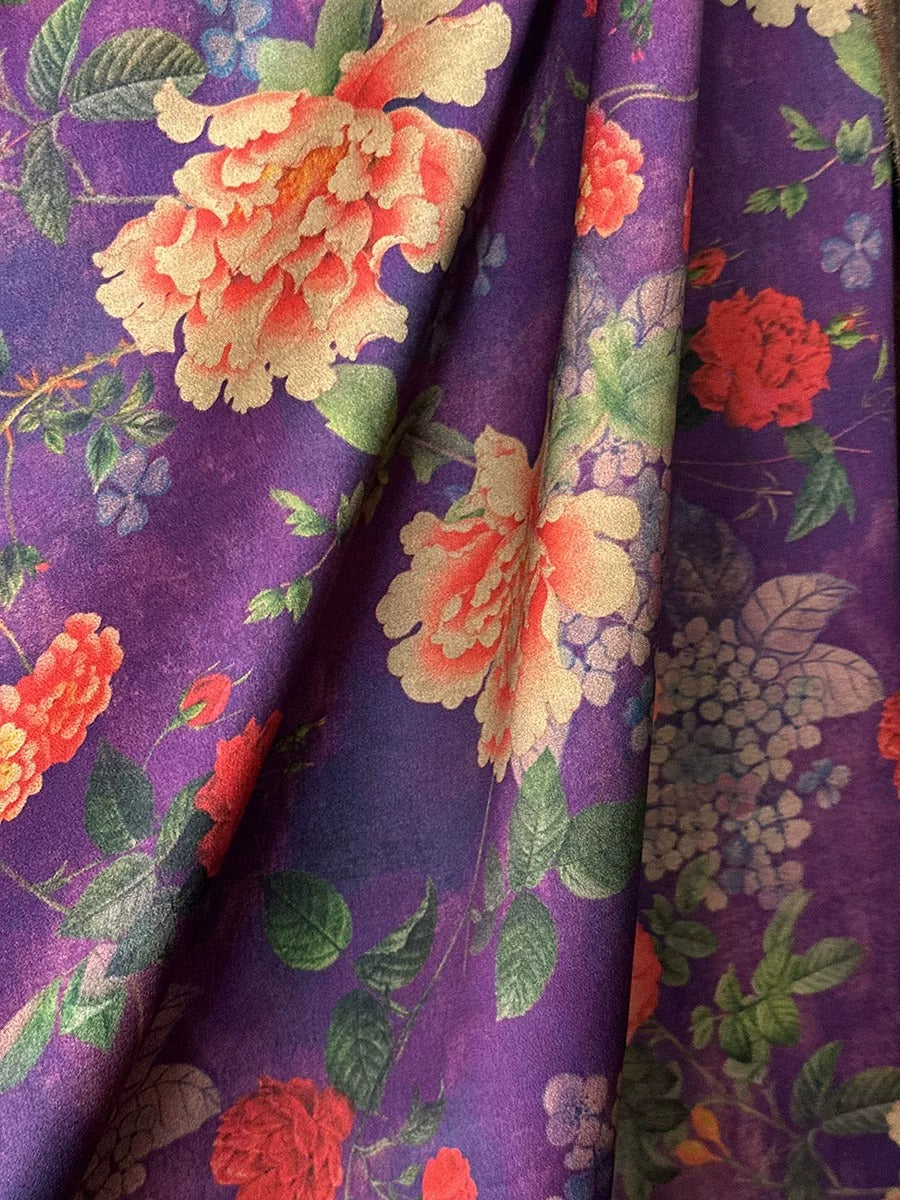 a close-up view of a fabric with a vibrant floral pattern in shades of purple, orange, and green. The fabric appears to be made of silk or a similar material, and the pattern is intricate and detailed, showcasing the craftsmanship of the design.