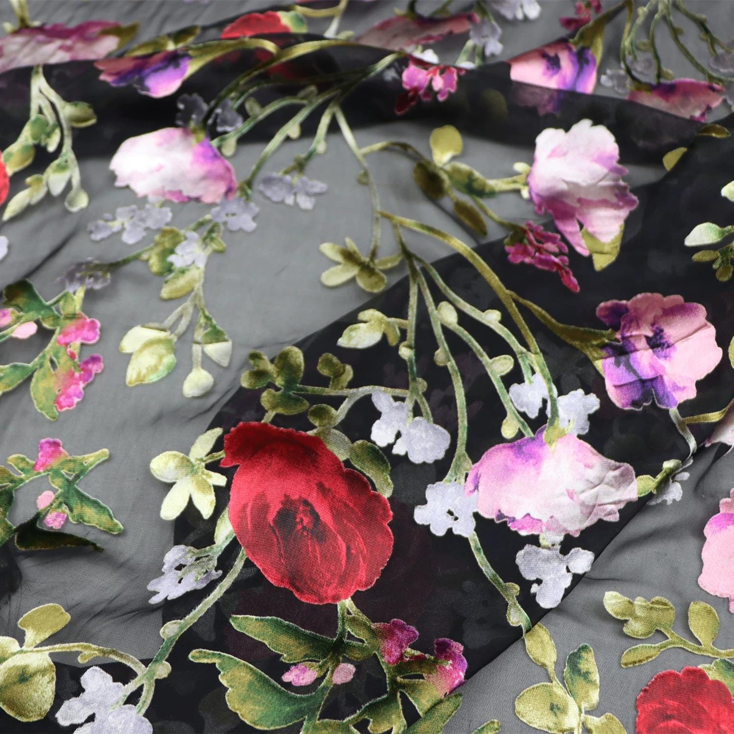 a close-up view of a fabric with a floral pattern, including red and pink flowers, green leaves, and white flowers. The fabric appears to be black, with the flowers and leaves creating a vibrant and colorful design.