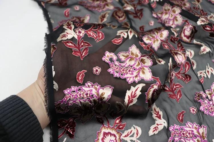 A hand is holding a fabric with a floral pattern in shades of red, pink, and white.