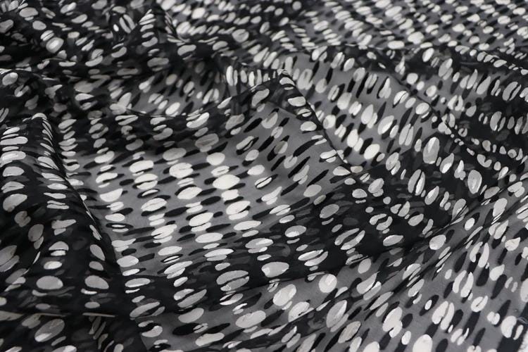 a close-up view of a fabric with a black and white polka dot pattern. The fabric appears to be made of sheer material, with a textured and wrinkled appearance.