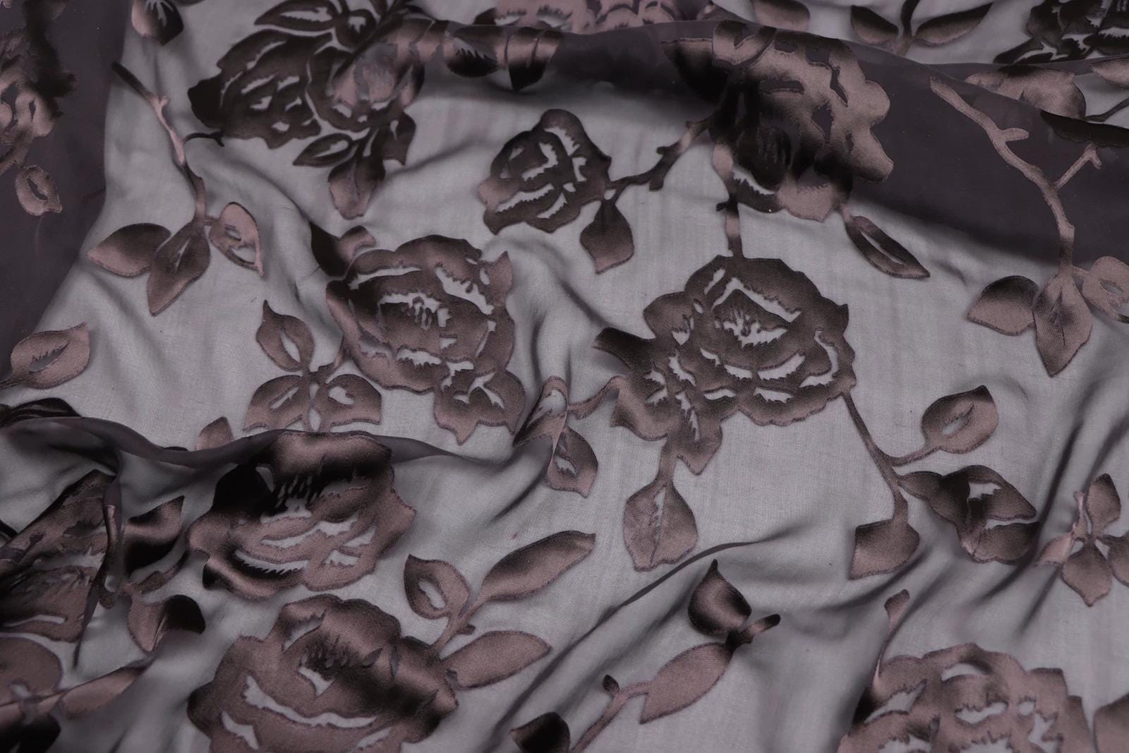 a close-up view of a fabric with a floral pattern, featuring dark brown or purple-colored flowers and leaves.