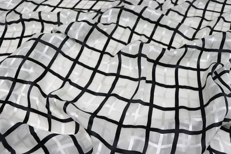 a close-up view of a fabric with a black and white checkered pattern. The fabric appears to be made of a sheer material, with a grid-like design that creates a visually striking pattern.