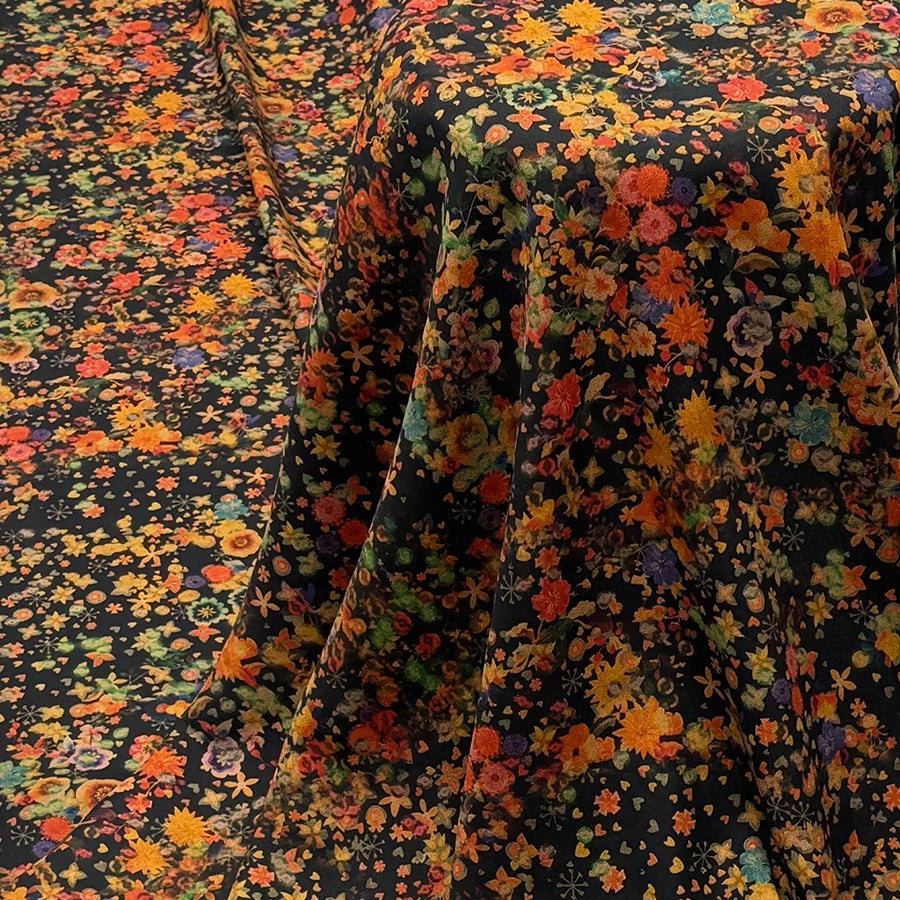 a close-up view of a fabric with a vibrant floral pattern in shades of orange, yellow, and green. The fabric appears to be black, providing a striking contrast to the colorful flowers. The fabric is folded and draped, creating a visually appealing display.