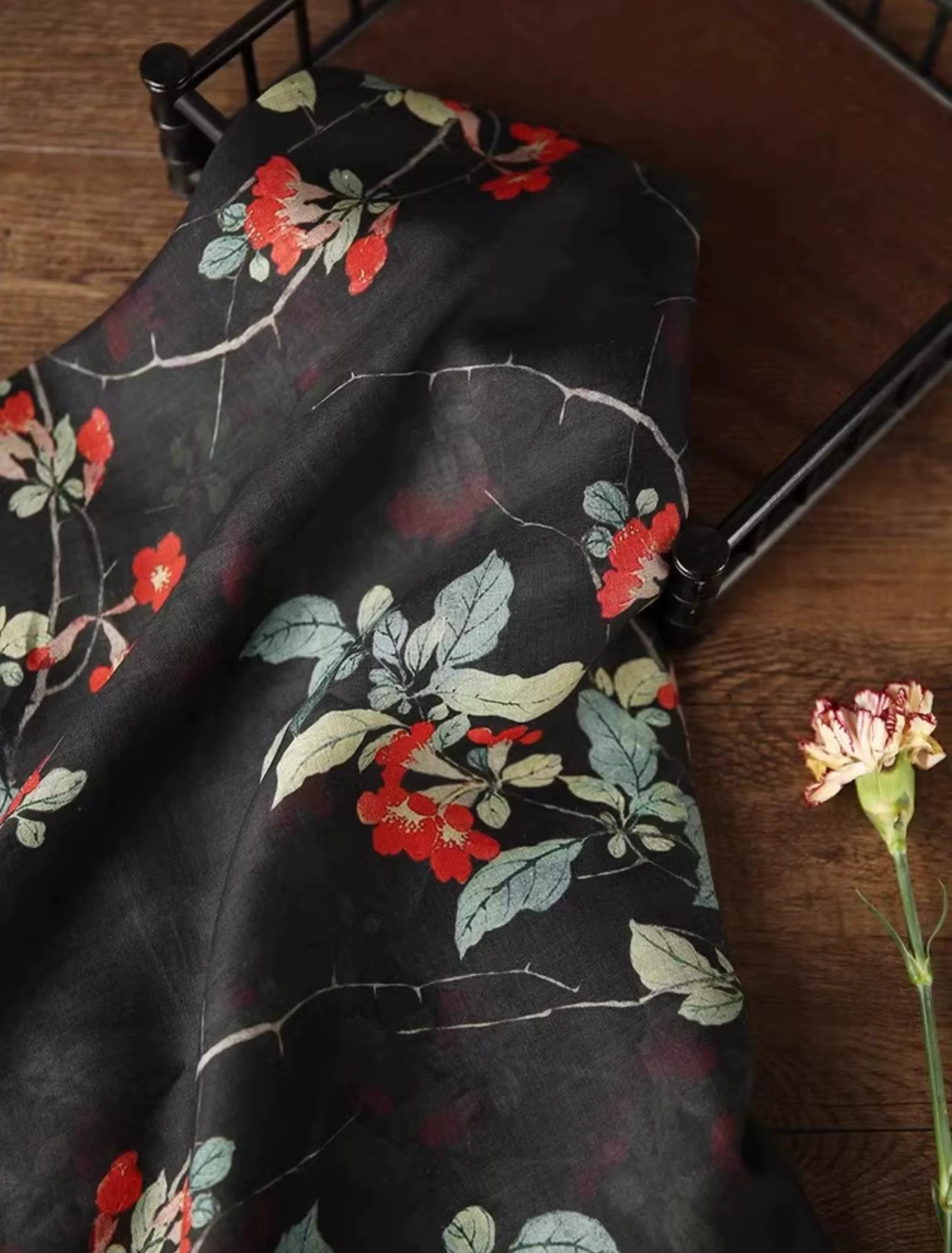 a black fabric with a floral pattern, including red and green flowers, and a single pink flower on a wooden surface.