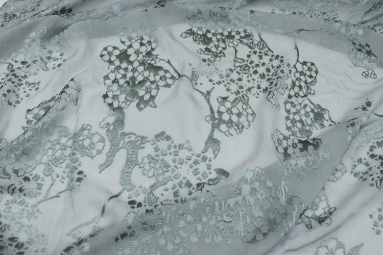 a close-up view of a fabric with a floral pattern, featuring a mix of white and gray colors.