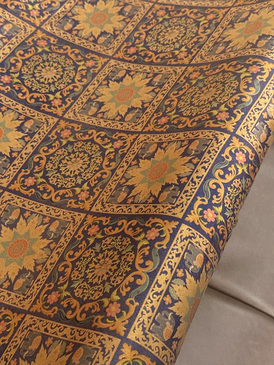 a close-up view of a fabric with a detailed floral pattern in shades of blue, gold, and yellow. The pattern consists of numerous small square designs, each with a unique flower motif, creating a visually striking and intricate design.