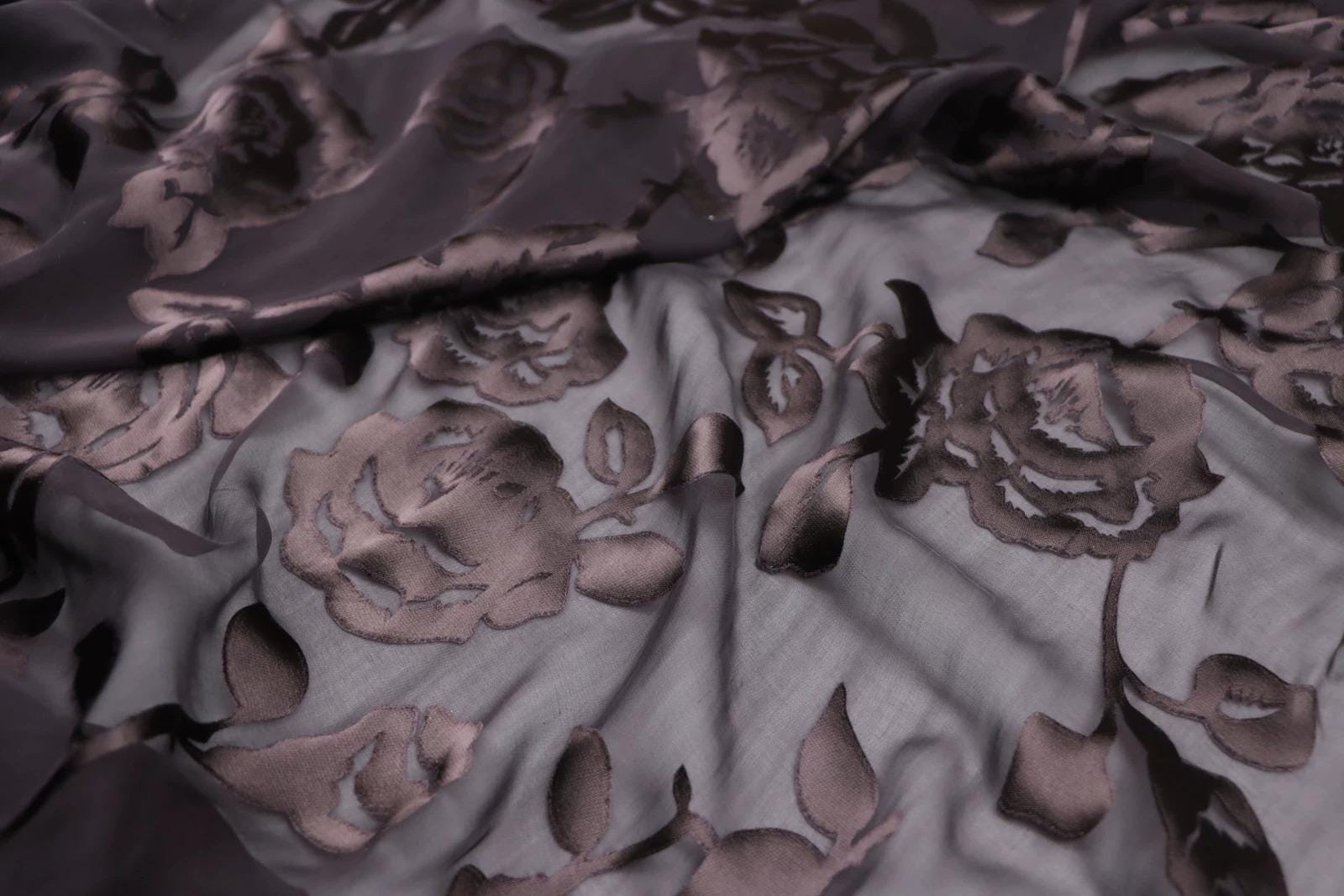 a close-up view of a fabric with a floral pattern, featuring dark brown or purple-colored flowers and leaves.