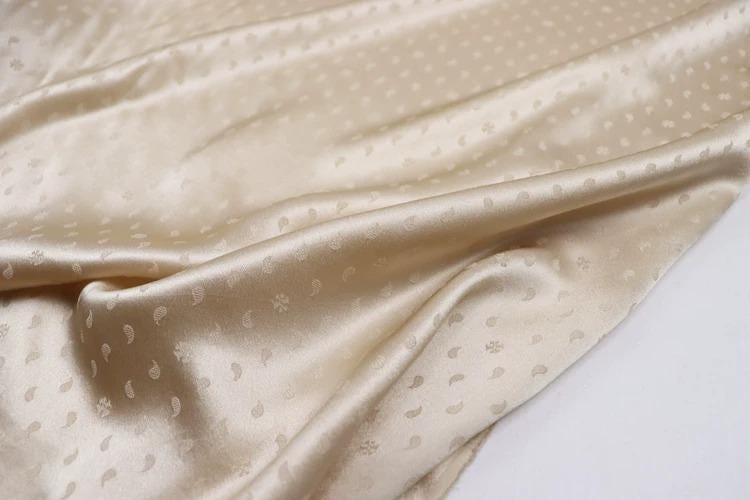 a close-up view of a fabric with a repeating pattern of small white dots or circles, creating a textured and shiny appearance.
