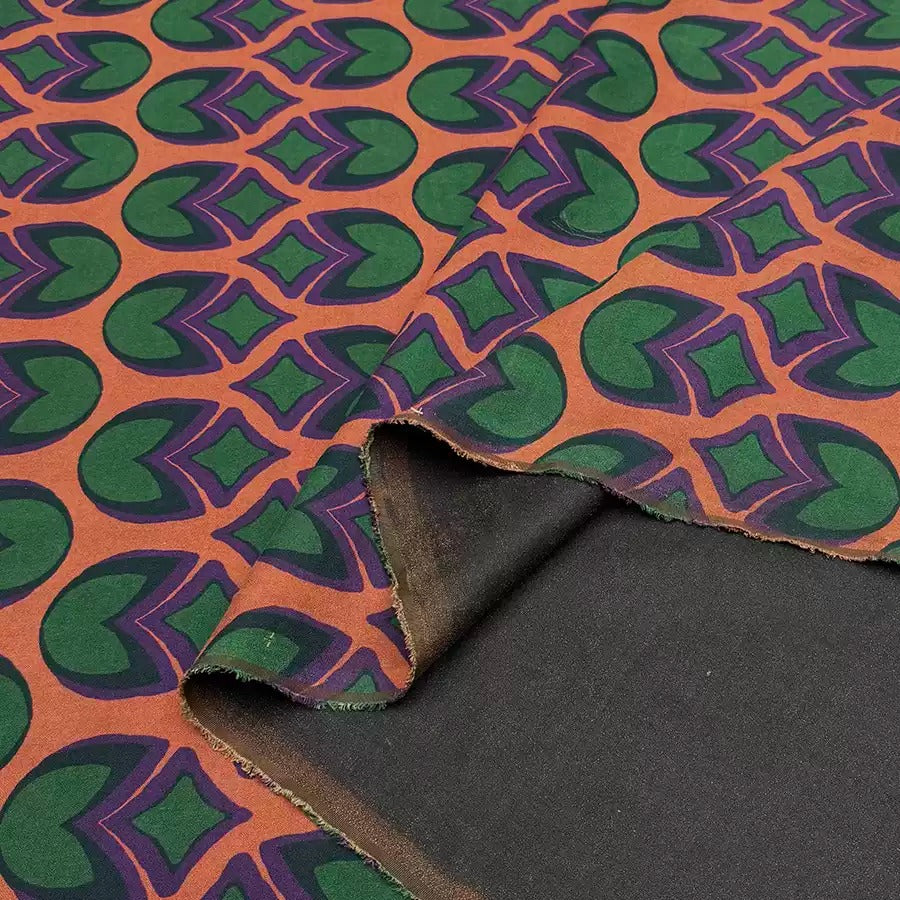 a close-up view of a fabric with a repeating pattern of green and purple circles on an orange background.