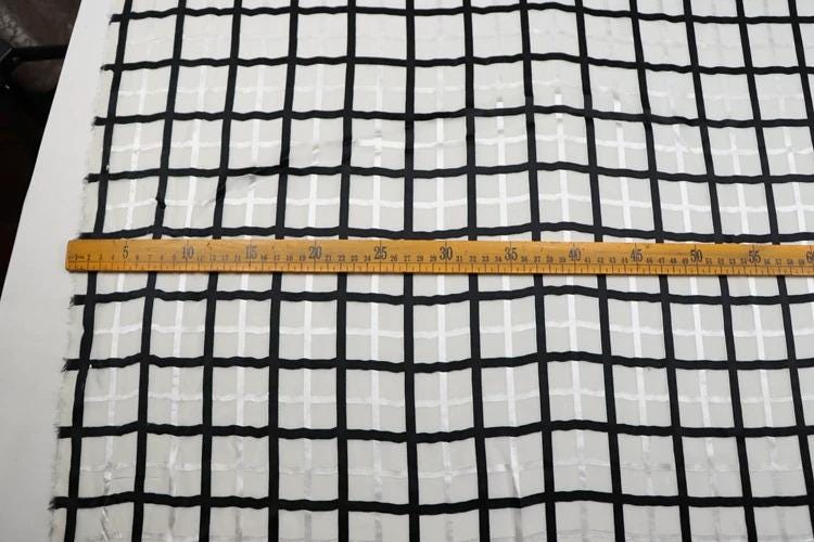a close-up view of a fabric with a grid pattern, and a ruler is placed across it to measure the length of the fabric.