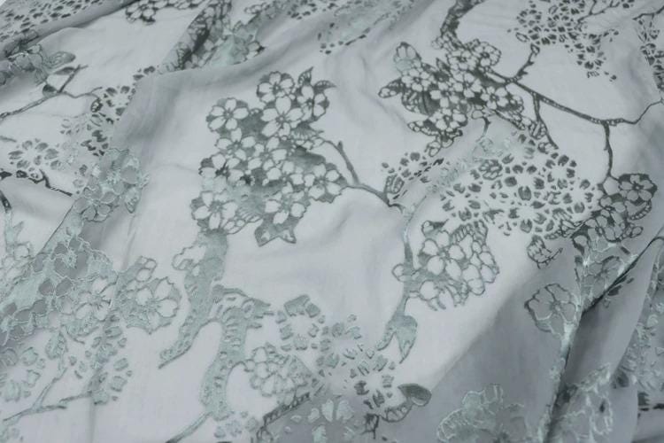 a close-up view of a fabric with a floral pattern, featuring a repeating design of white flowers against a light gray background.
