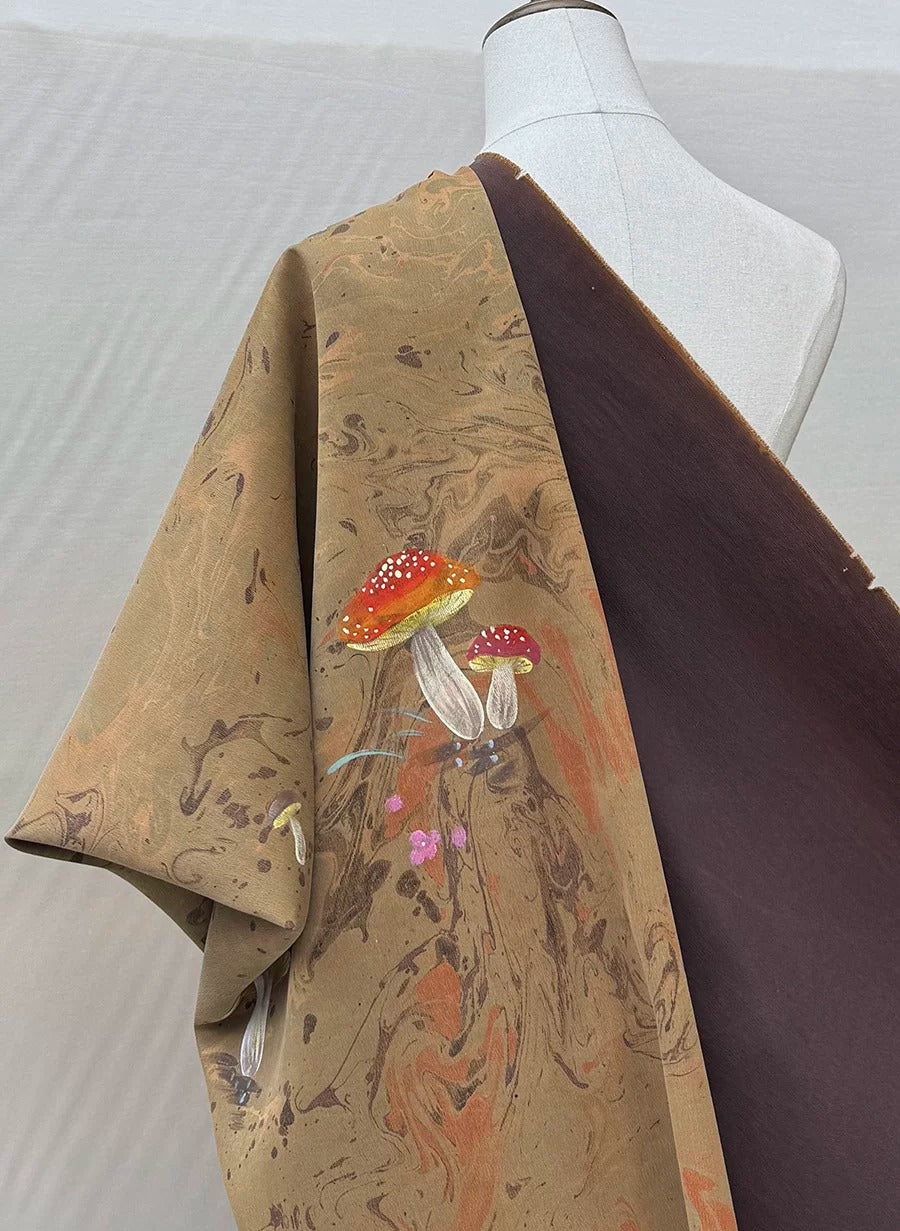 A mannequin wearing a brown and orange patterned fabric with mushrooms and other natural elements.
