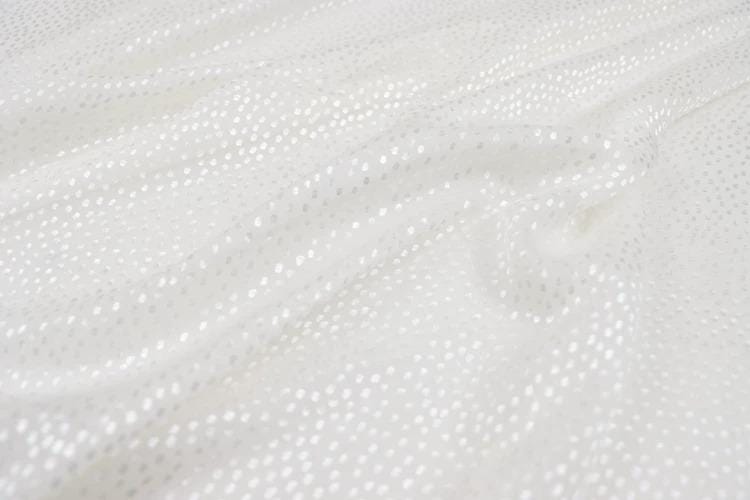 a close-up view of a white fabric with small white dots or polka dots, creating a textured and shiny appearance.