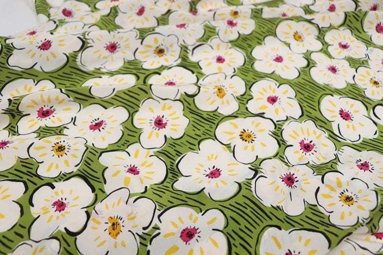 a close-up view of a fabric with a repeating pattern of white flowers with yellow centers against a green background.