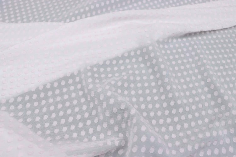 a close-up view of a fabric with a white polka dot pattern. The fabric appears to be a sheer material, with a white background and a white dotted pattern. The fabric is crumpled, giving it a slightly wrinkled appearance.