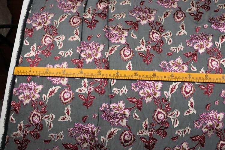 a fabric with a floral pattern, and there is a yellow measuring tape placed across it, indicating the size of the fabric.