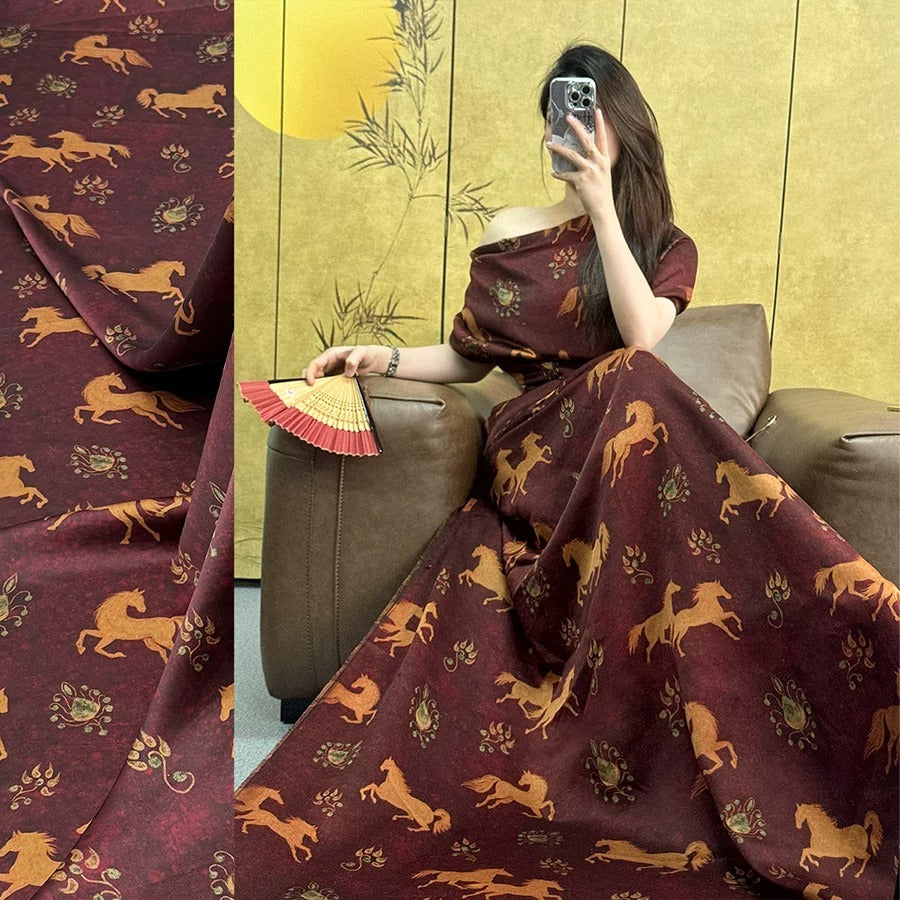 A woman is sitting on a couch, wearing a long dress with a pattern of horses, and holding a fan.