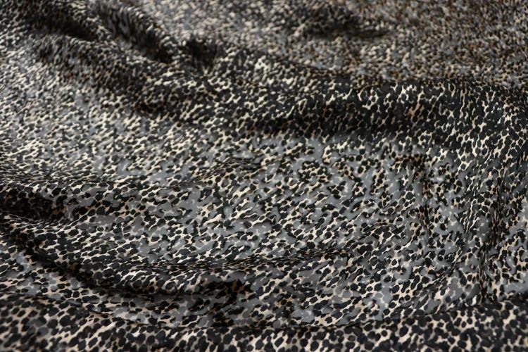 a close-up view of a fabric with a distinctive leopard print pattern. The fabric appears to be a dark-colored material with a mix of black and white spots, creating a visually striking and textured appearance.