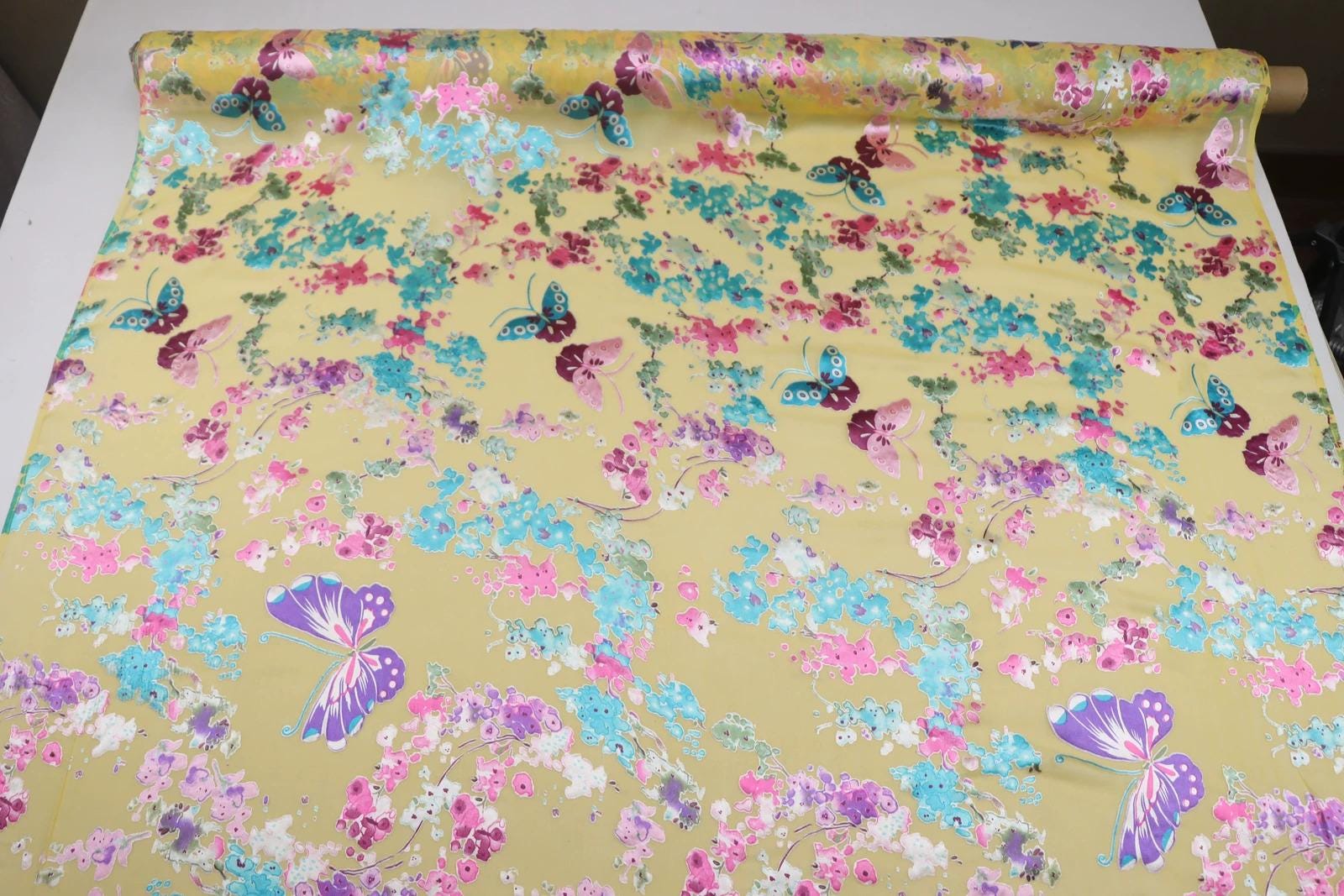 a vibrant, colorful fabric with a repeating pattern of butterflies and flowers in shades of pink, blue, and green. The fabric appears to be a piece of clothing or textile, with the butterflies and flowers adding a lively and playful touch to the design.