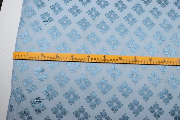 a blue fabric with a repeating pattern of blue flowers, and a yellow measuring tape is placed across the fabric, indicating the size of the fabric.
