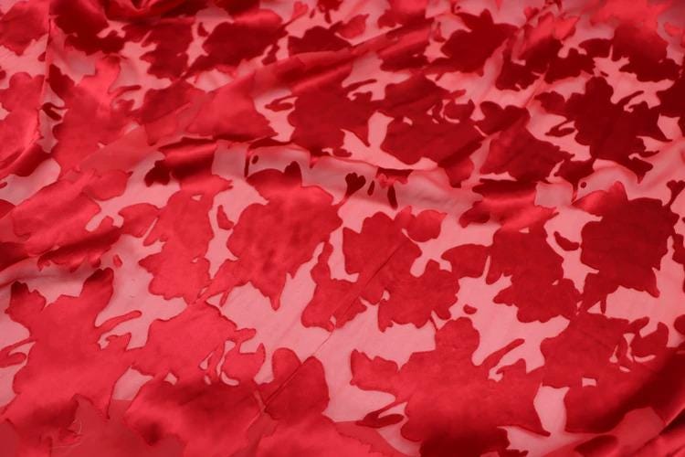 a close-up view of a fabric with a red floral pattern. The fabric appears to be made of a shiny, shiny material, possibly silk or satin, and has a slightly wrinkled texture. The pattern consists of red flowers or leaves, which are the main design element of the fabric. The image does not contain any text or other objects, and the focus is solely on the fabric and its floral pattern.