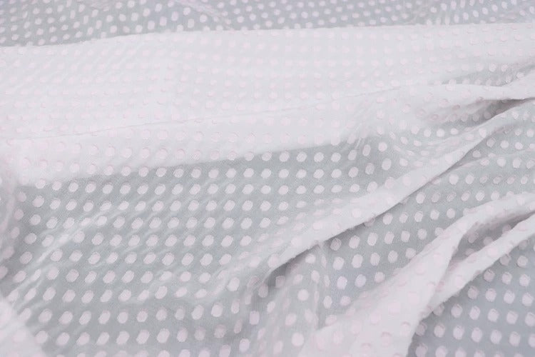 A close-up view of a fabric with a white polka dot pattern, with the fabric appearing crumpled and wrinkled.