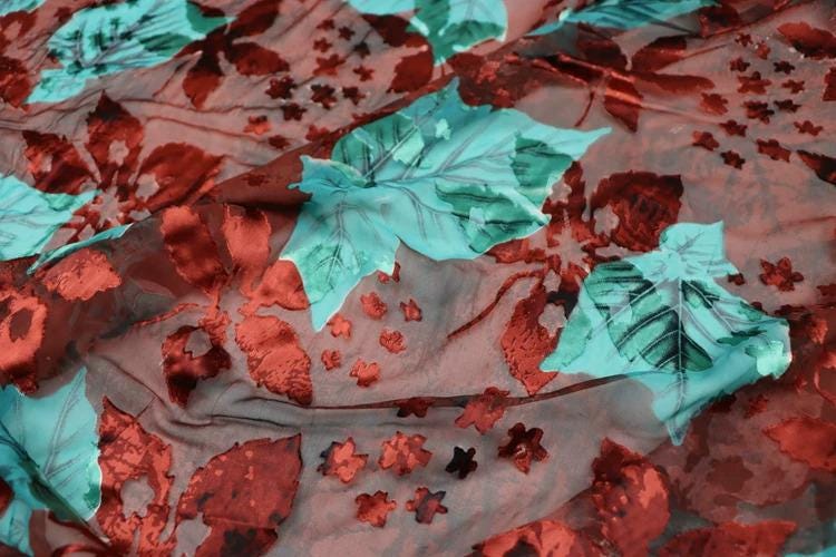 a close-up view of a fabric with a floral pattern. The fabric has a mix of red and green leaves, along with small red flowers, creating a vibrant and colorful design. The pattern appears to be a close-up of the fabric, showcasing the intricate details and textures of the leaves and flowers.
