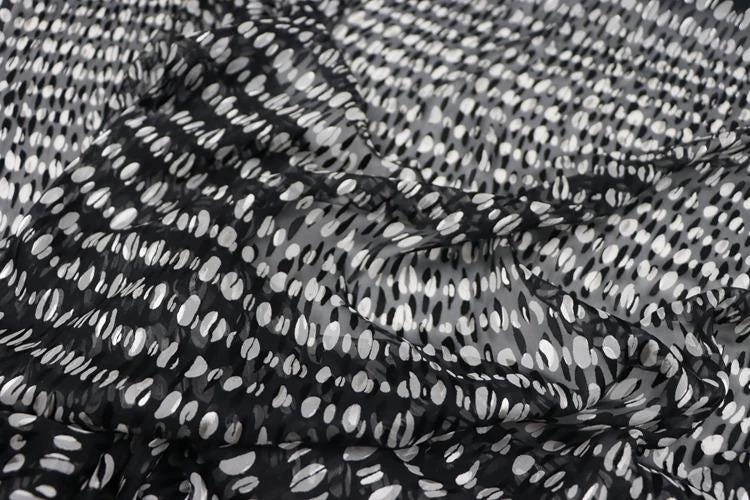 a close-up view of a fabric with a black and white polka dot pattern. The fabric appears to be made of a sheer material, with a textured and wrinkled appearance.