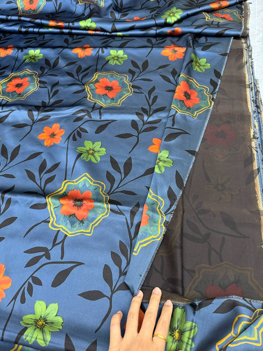 a hand holding a piece of fabric with a floral pattern on it. The fabric appears to be a dark blue color with orange and green flowers and leaves. The hand is positioned in front of the fabric, suggesting the person is holding or touching it.