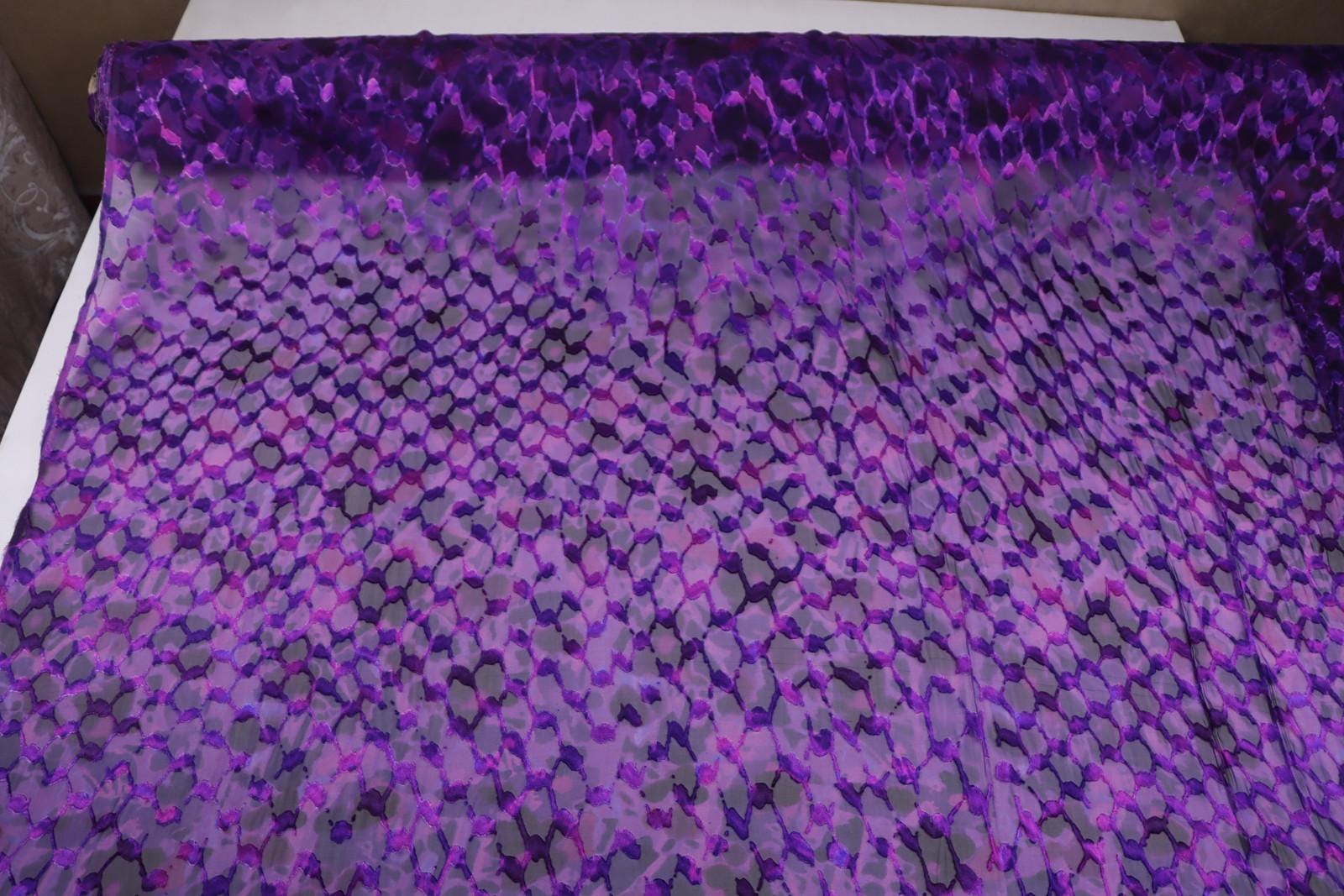 a close-up view of a fabric with a purple and black pattern, featuring a repeating geometric design.