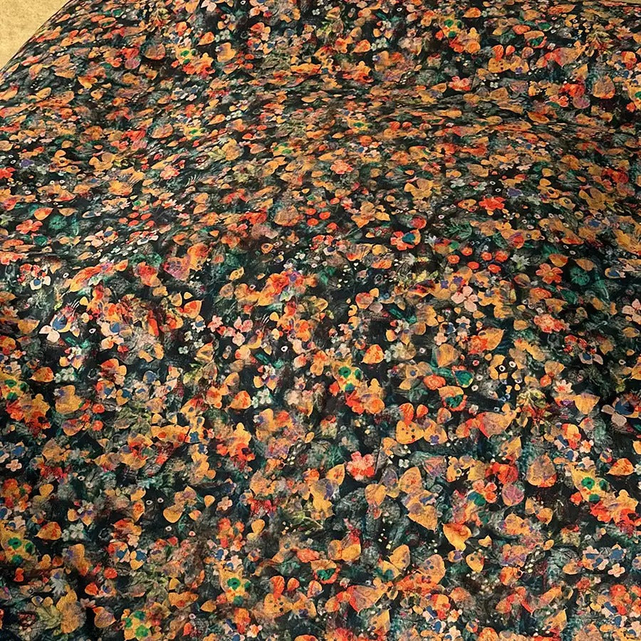 The image is a close-up of a fabric with a vibrant, colorful floral pattern. The fabric appears to be a blend of various shades of green, orange, and yellow, creating a visually striking and intricate design.