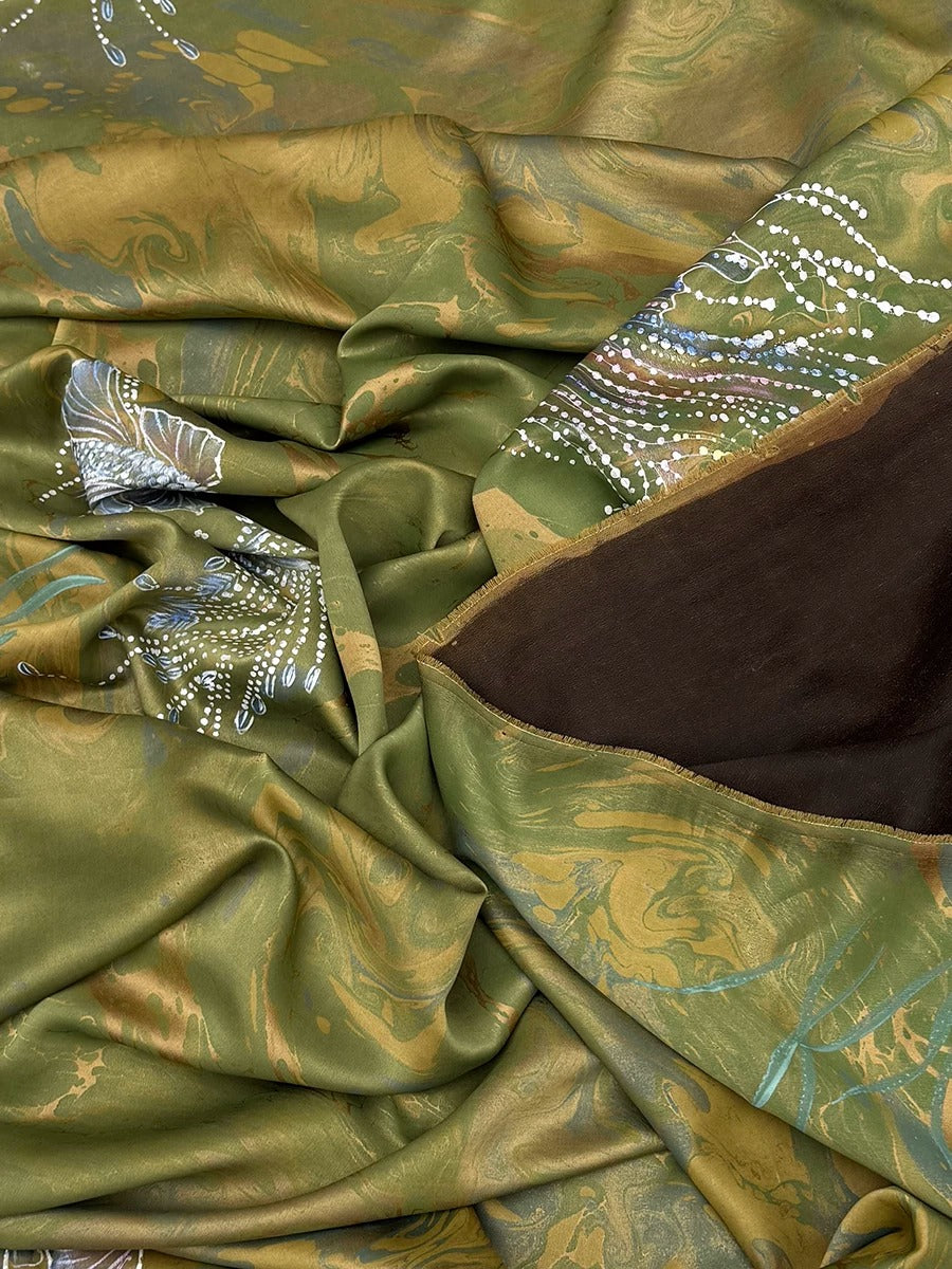 The image is a close-up view of a fabric with a green and brown color scheme, featuring a pattern of swirls and dots. The fabric appears to be made of silk or a similar material, and it is crumpled, giving it a textured and wrinkled appearance.