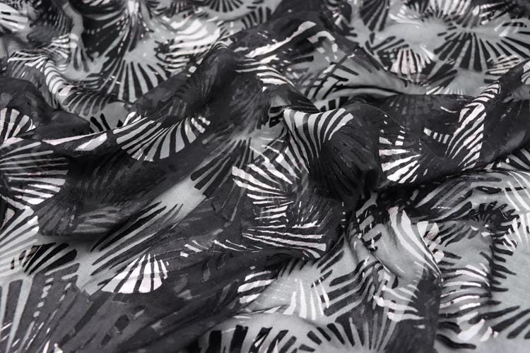 a close-up view of a fabric with a black and white abstract pattern, featuring a repeating design of black and white lines and shapes.