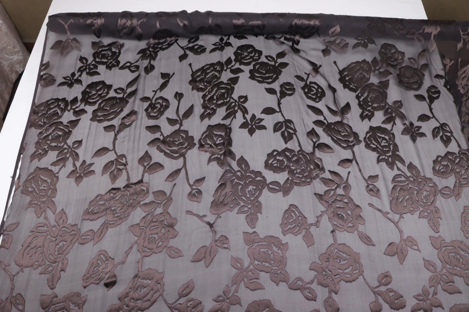 a close-up view of a fabric with a floral pattern, featuring a repeating design of roses and leaves.