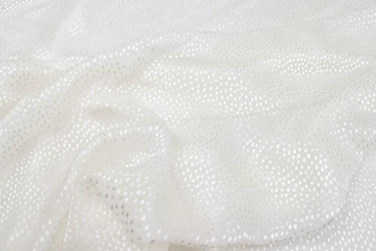 a close-up view of a white fabric with small white dots or sequins, creating a textured and shiny appearance.